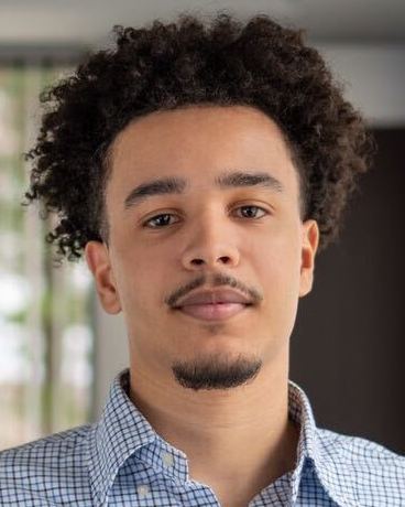 Young man with short curly black hair and light brown skin wearing a button down oxford shirt.