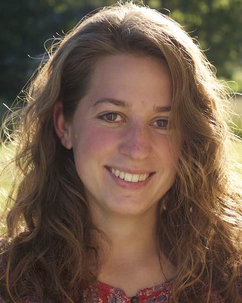 Young woman smiling with sunlight reflecting off of her long curly hair smiling at the camera.