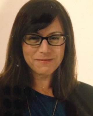 A dark haired woman with a wry grin and designer, black glasses. 