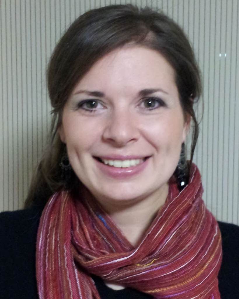 Woman with a large, friendly smile, long brown hair and a stylish red and multi color scarf.